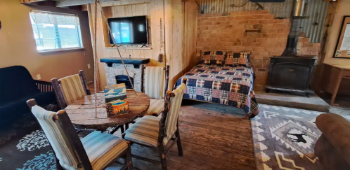 Cozy interior featuring a bed, dining table, and rustic decor with a wood stove and TV.